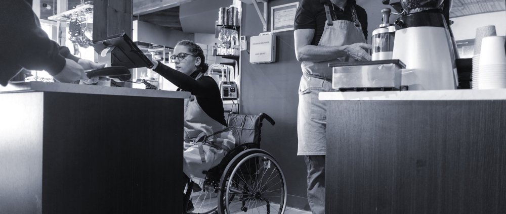 A woman in a wheelchair operating a POS terminal at a cafe